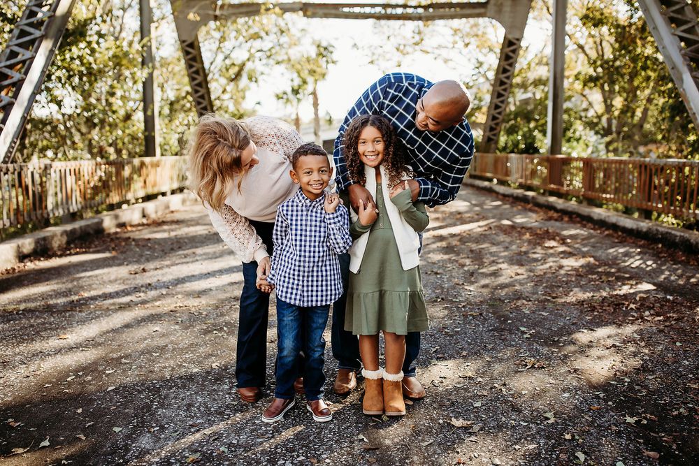 A family walks together on a tree-lined dirt path on a bright sunny day during a lifestyle portrait session.