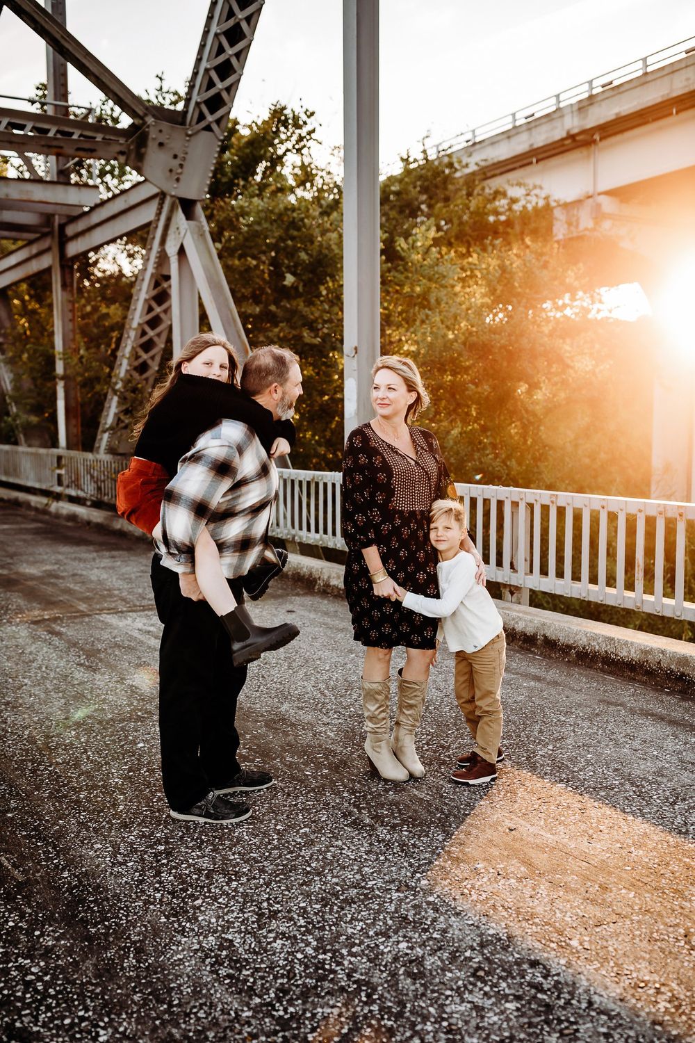 A family shares a joyful moment together at sunset on a bridge with metal beams visible in the background.