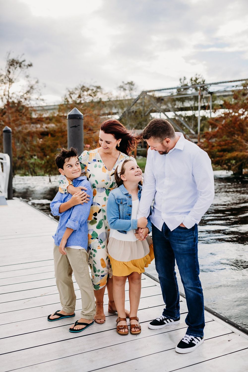 A laughing family shares a candid moment together on a wooden dock by the water on a cloudy autumn day.
