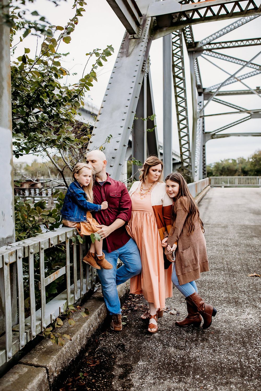 A happy group poses together against a metal bridge structure during an autumn photoshoot.