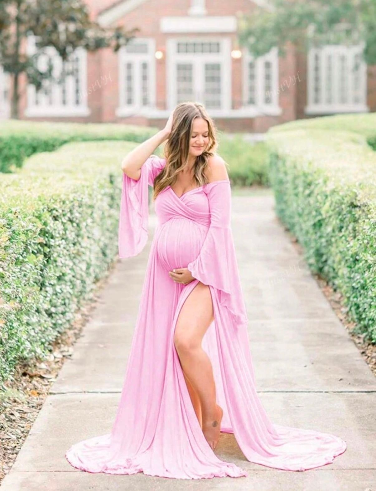 A flowing pink maternity dress creates movement along a garden pathway.