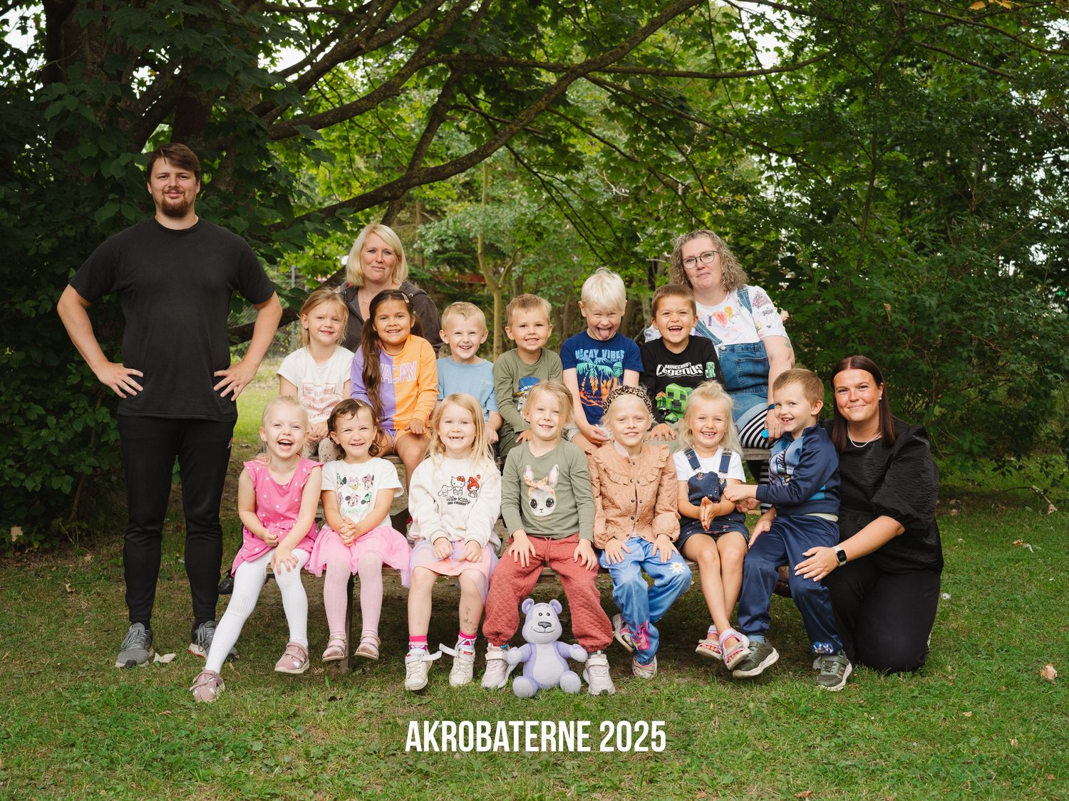 A group of children and adults pose together for an outdoor family photo session in a lush green park setting.