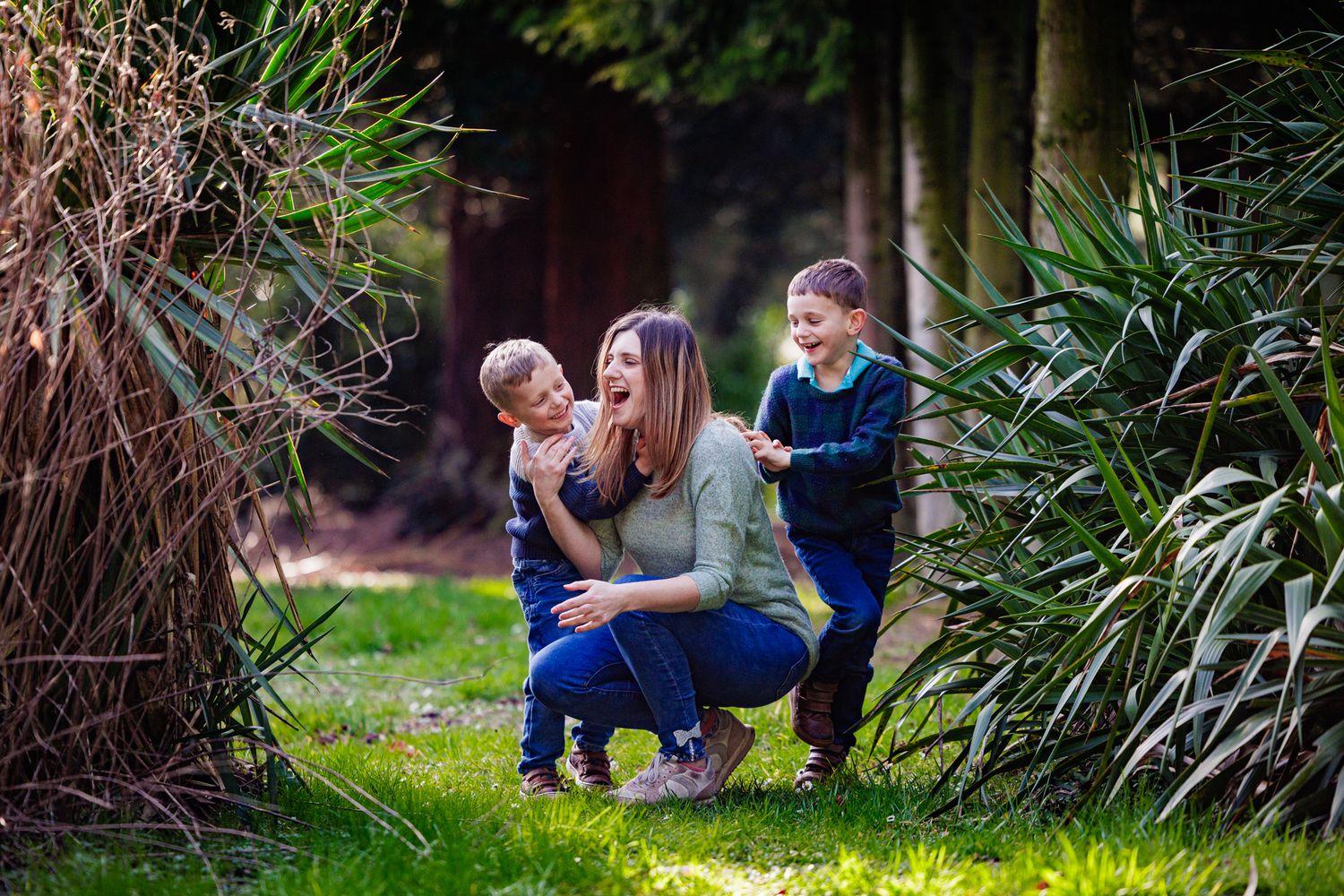 A family shares a tender moment outdoors between ornamental grasses on a sunny afternoon in a garden setting.