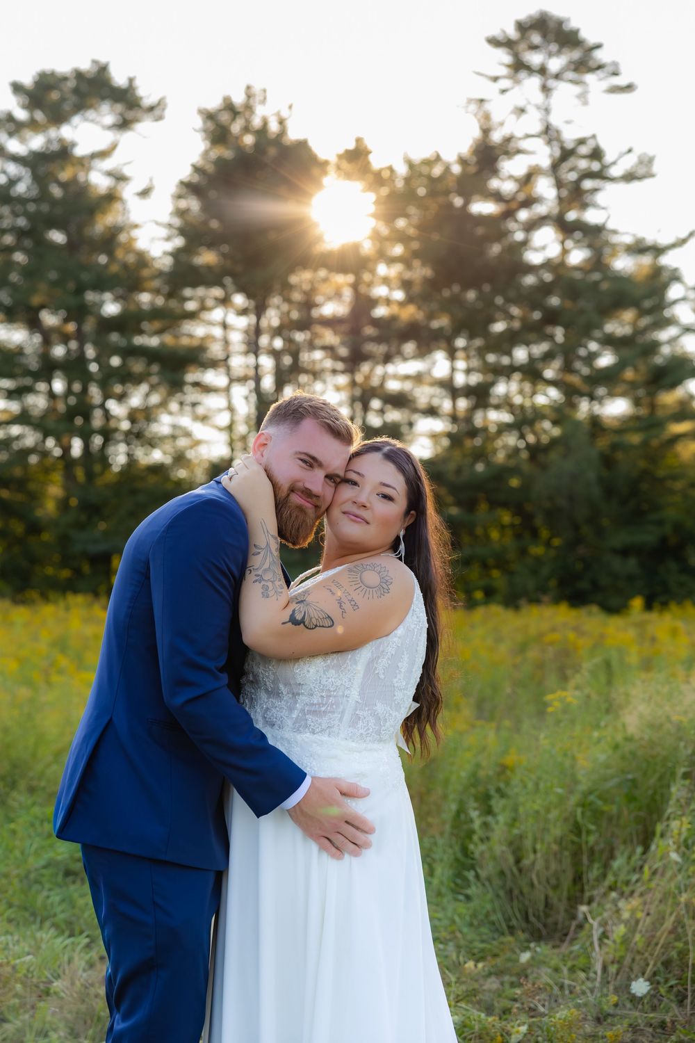 Happy couple shares romantic kiss in dreamy outdoor setting with evergreen trees and golden sunset.