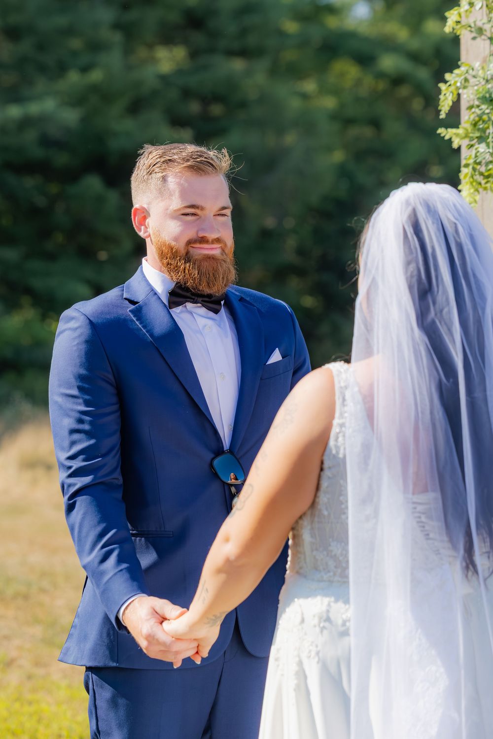 A touching moment between newlyweds as they share vows outdoors, with the groom in a navy suit and bowtie.