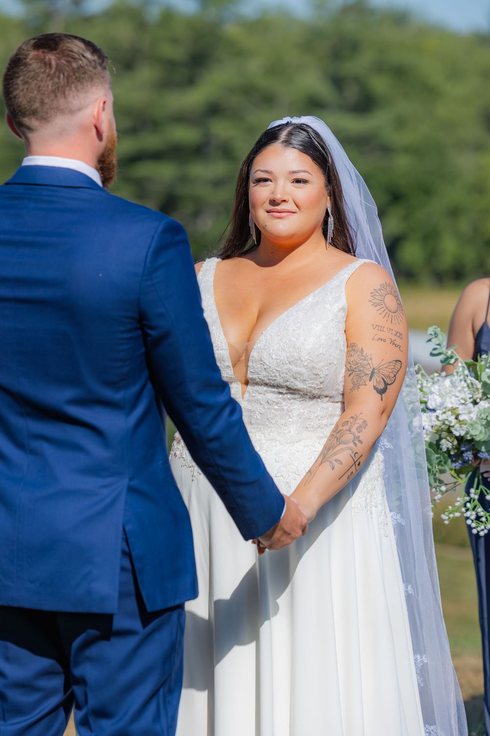 A wedding couple at an outdoor ceremony wearing a traditional white dress and navy blue suit during a first look moment.