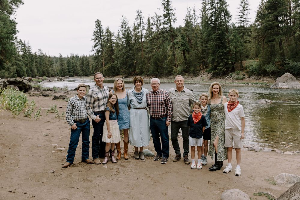 Group portrait session by a river with pine trees and mountains in the background.