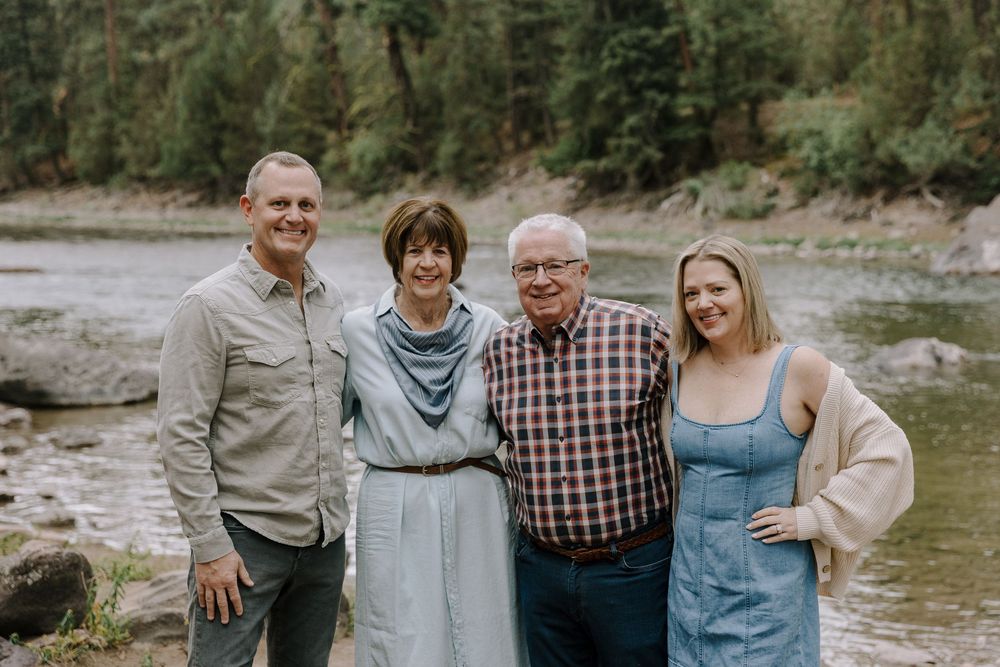 Family gathering by a rocky riverbank surrounded by evergreen forest.