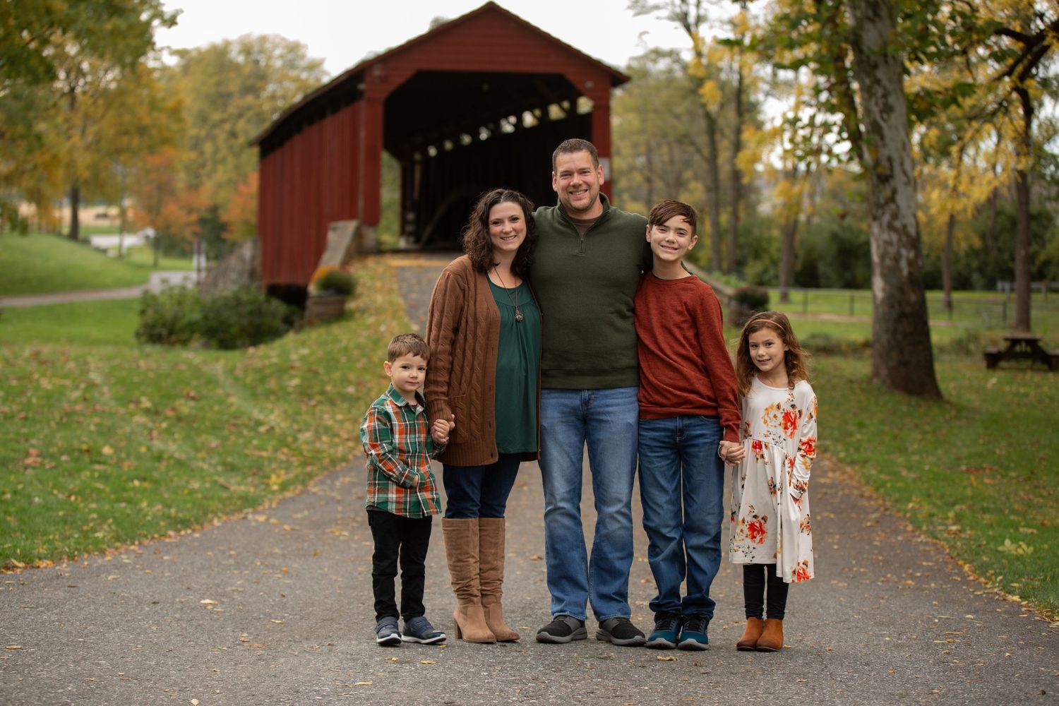 Family autumn portrait session near rustic red barn with fall foliage.