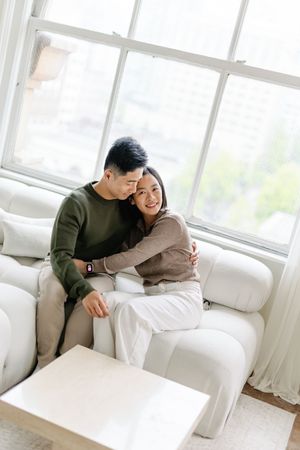 A romantic couple shares tender moments together on a white couch in a bright, sunlit living room.
