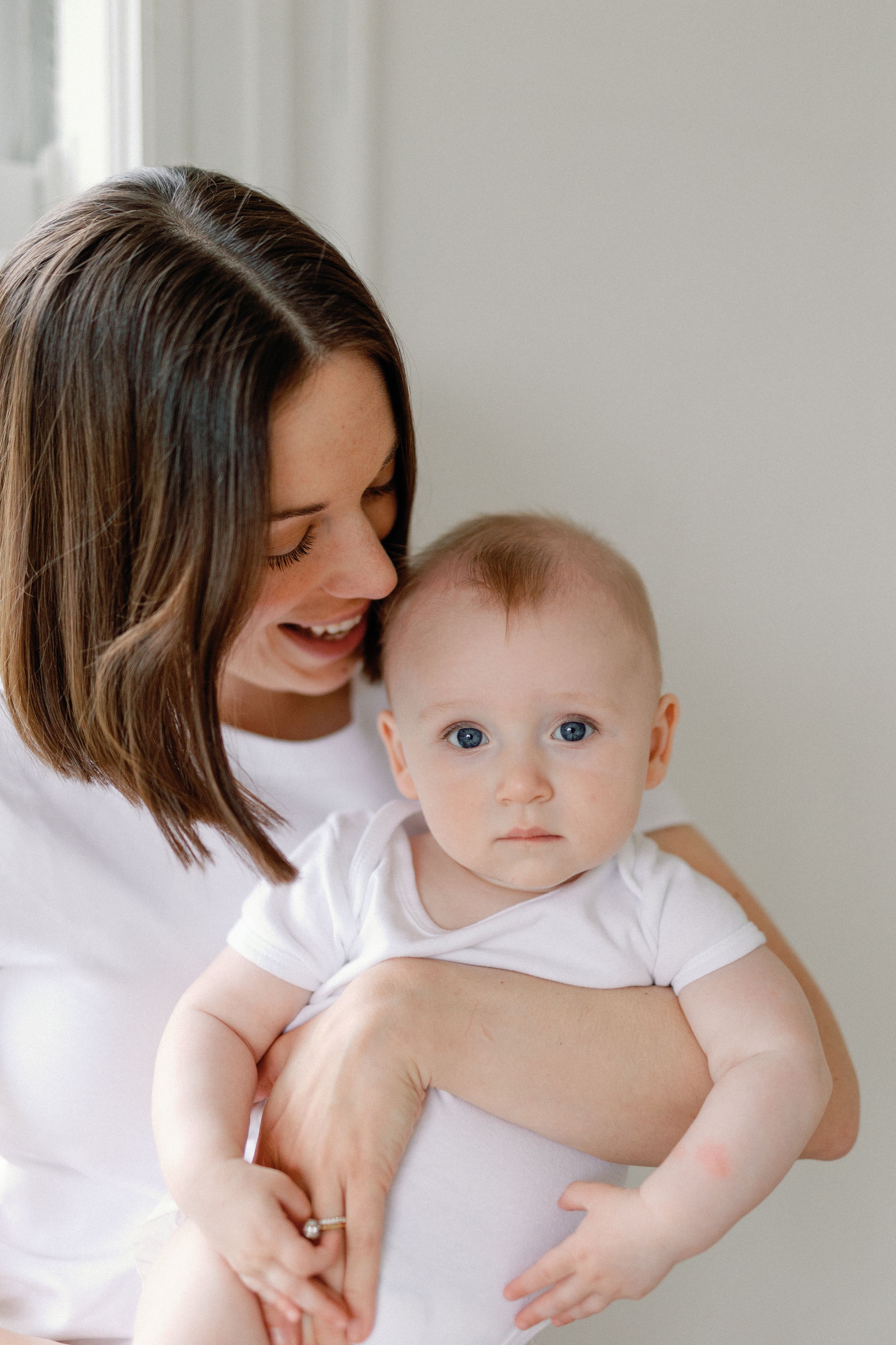 A series of four tender moments between a parent and baby wearing white, showing loving embraces and gentle affection.