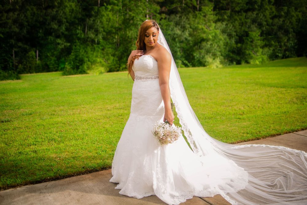 A bride in a flowing white dress poses on a lush green lawn during sunset.