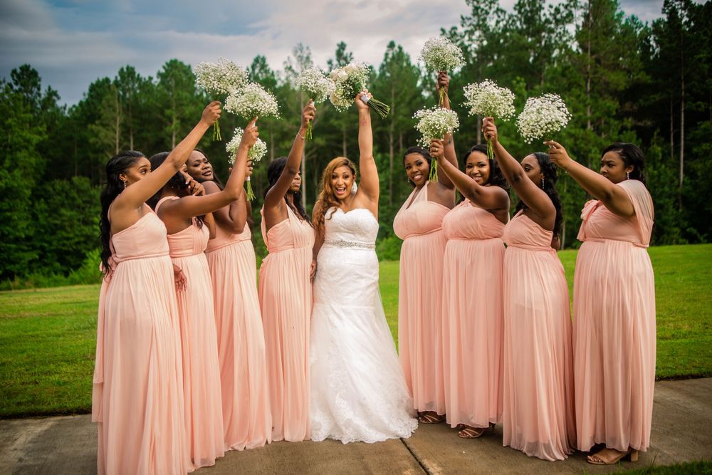 Wedding party wearing pink bridesmaid dresses poses together outdoors.
