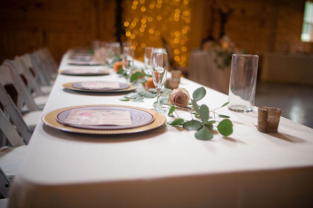 Elegant place settings with silver chargers and greenery at a wedding reception.