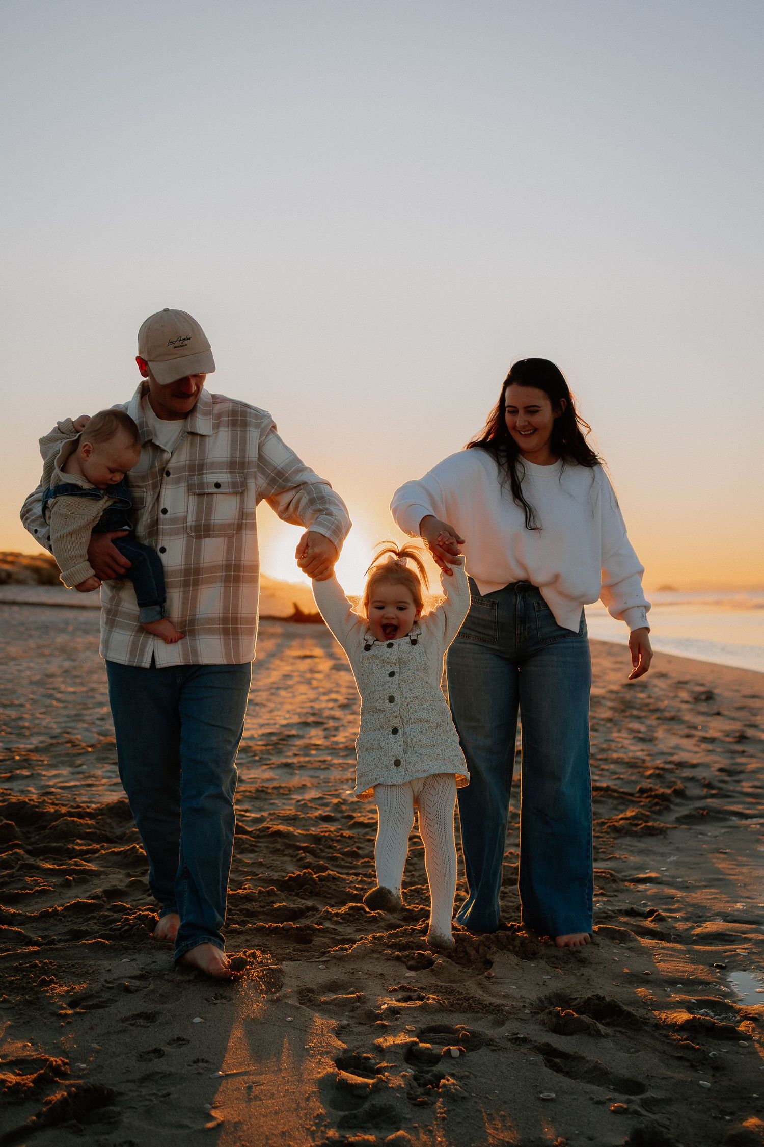 A family shares tender moments while playing together on a sandy beach at sunset.