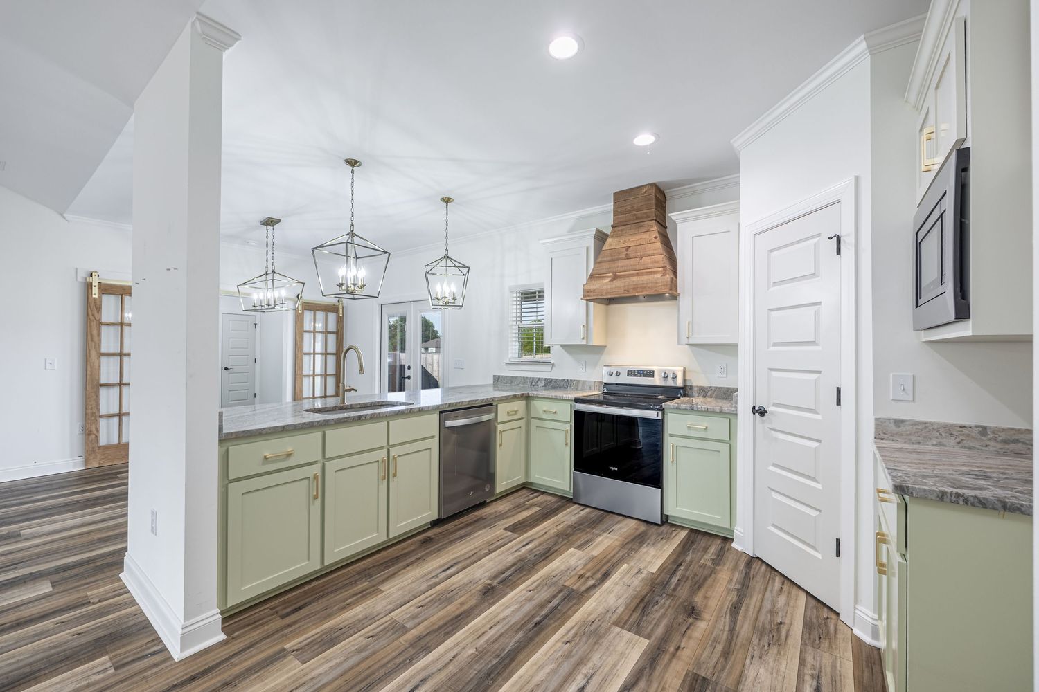 Modern open concept living space with white kitchen island, gray hardwood floors and ceiling fan in bright interior.