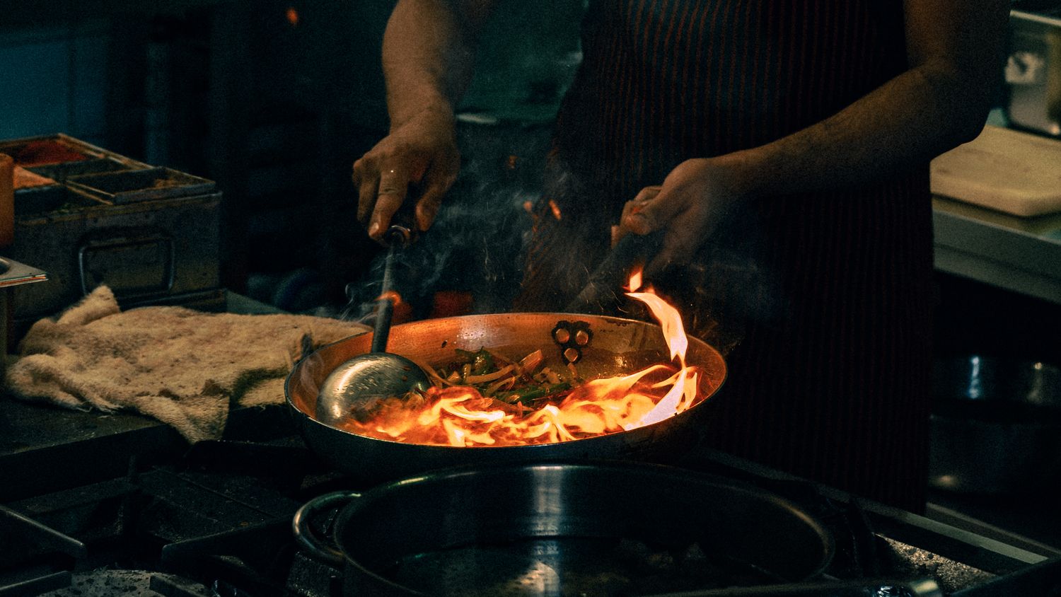 Fresh ingredients being sautéed in a pan on a professional kitchen stovetop.