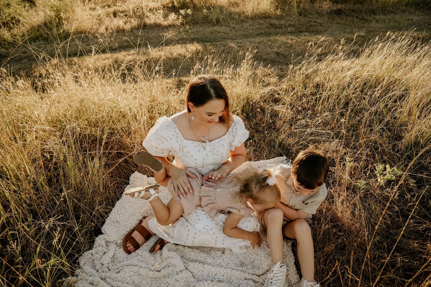 Family in white outfits embracing during sunset in a golden wheat field during outdoor photography session.
