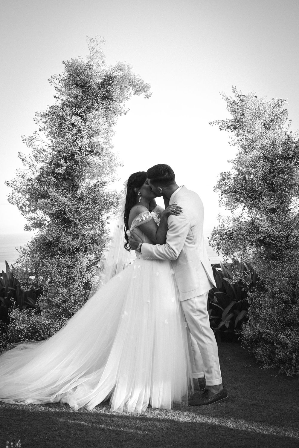 A romantic black and white series shows a couple in bridal attire embracing against a backdrop of trees in five similar poses.