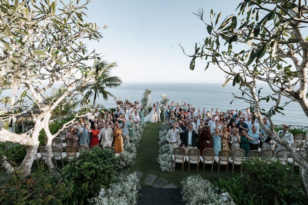 White folding chairs set up for outdoor wedding ceremony under rustic wooden arch decorated with flowing white fabric.