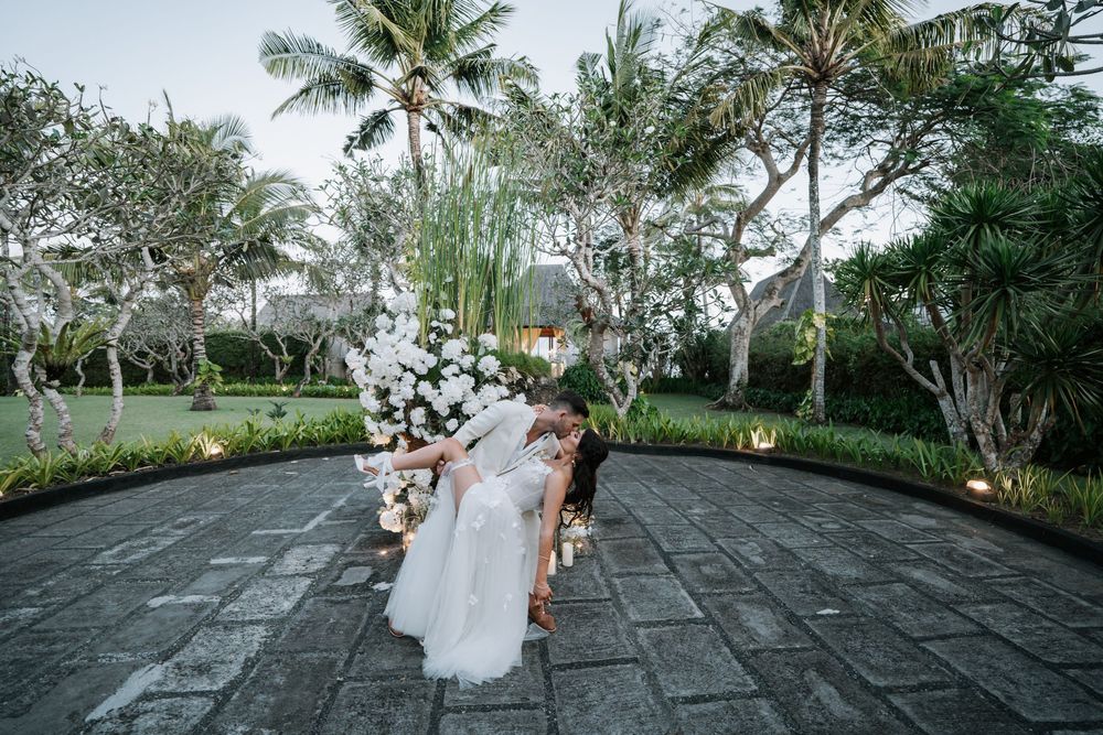 A wedding couple dances romantically under swaying palm trees at a tropical outdoor venue during sunset.