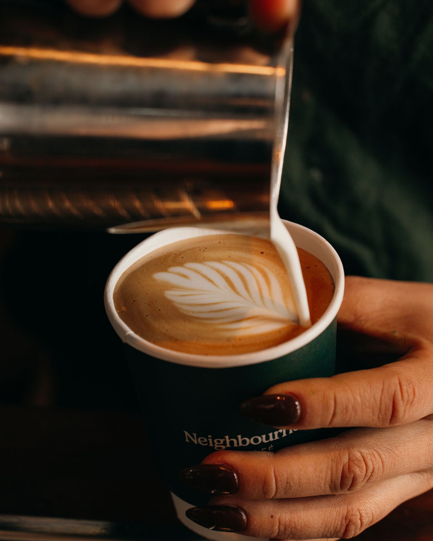 Barista pouring steamed milk into a latte creating a delicate leaf pattern in the foam.