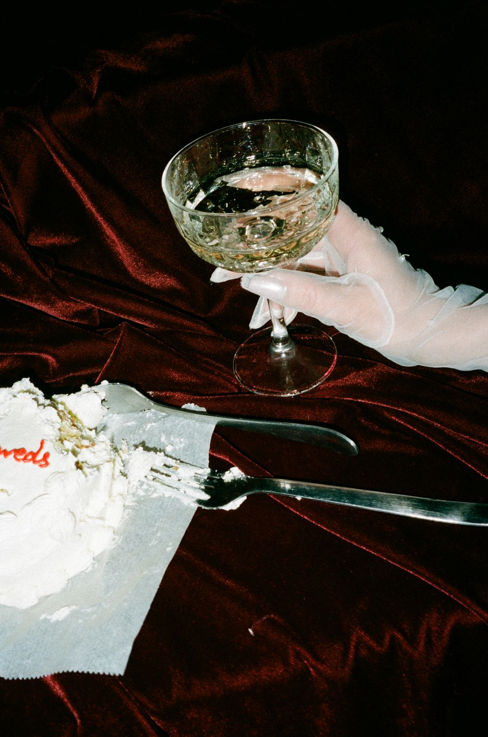 A hand holds an elegant martini glass against a dark red velvet surface.