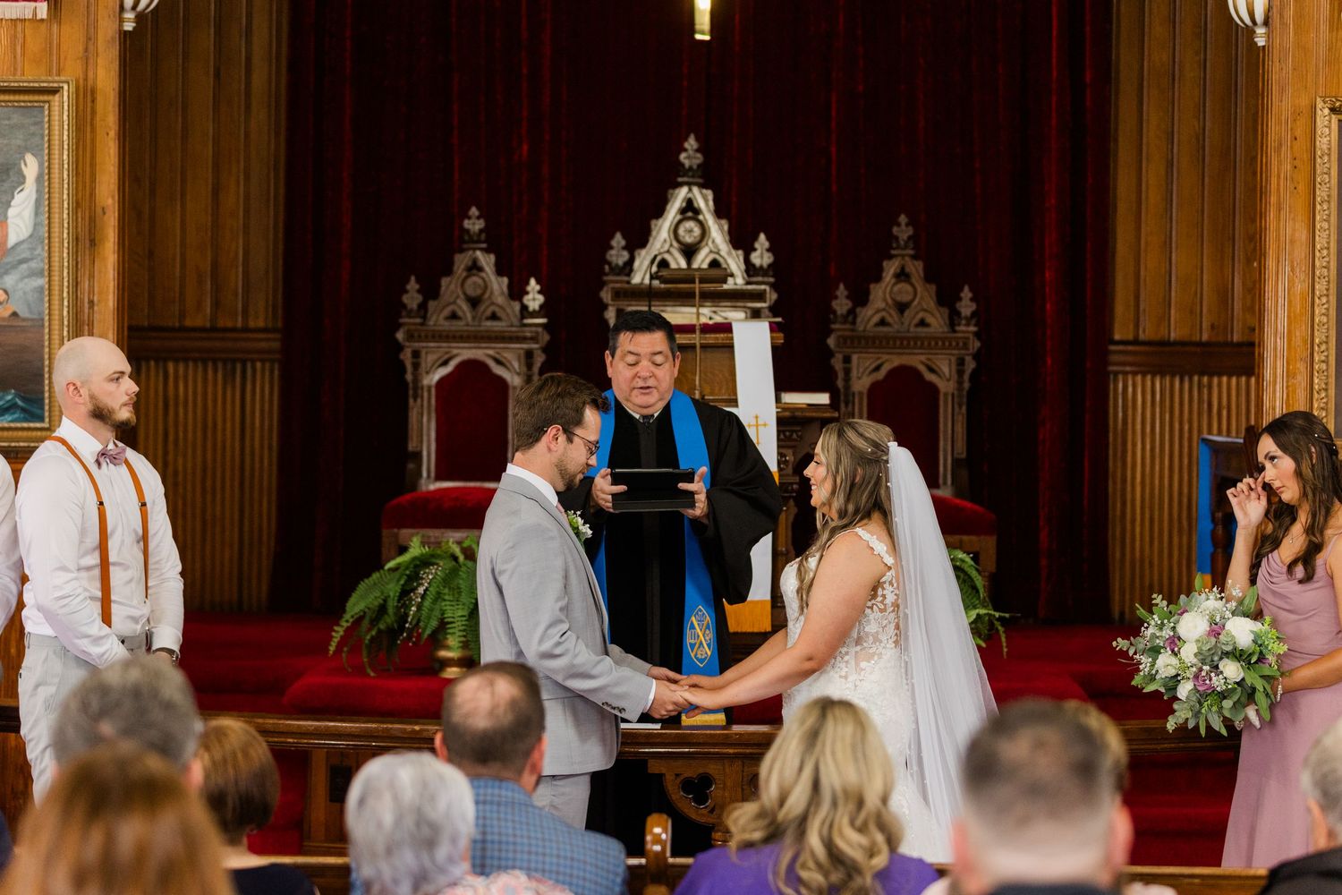 Wedding party and guests gather in an ornate wood-paneled church sanctuary during a celebration ceremony.