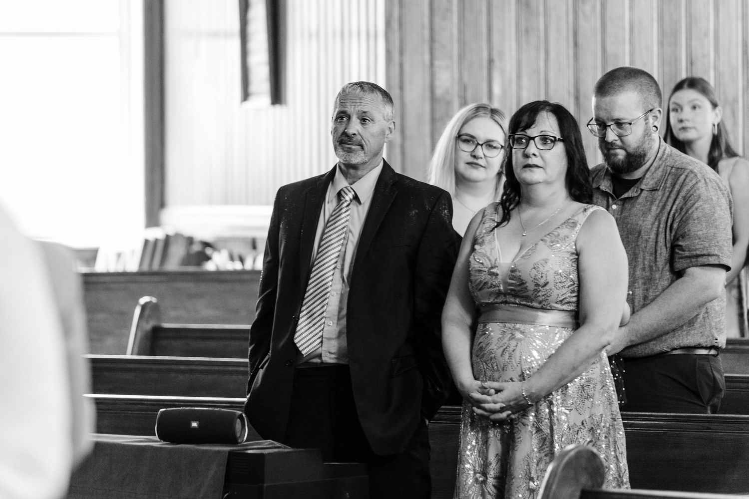 A black and white wedding photo shows family members seated in church pews during a ceremony.