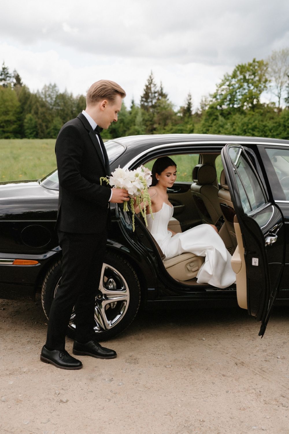 Elegant black wedding car with formal couple entering the vehicle.