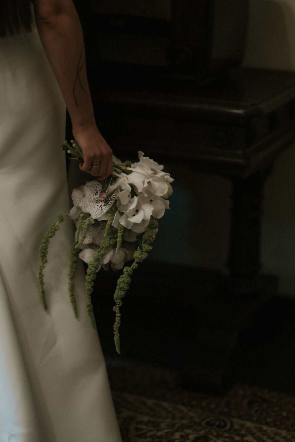 Close-up of white bridal bouquet with cascading greenery against white dress.