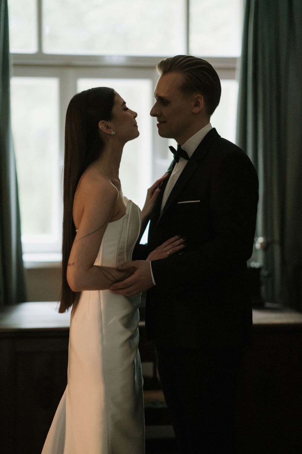 Silhouetted couple shares an intimate moment against bright windows in an elegant room.