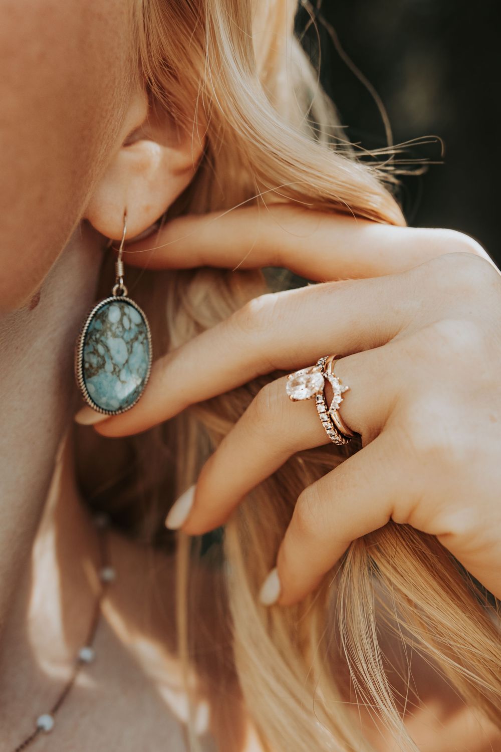 Close-up of turquoise jewelry earrings and rings with delicate hands against blonde hair.