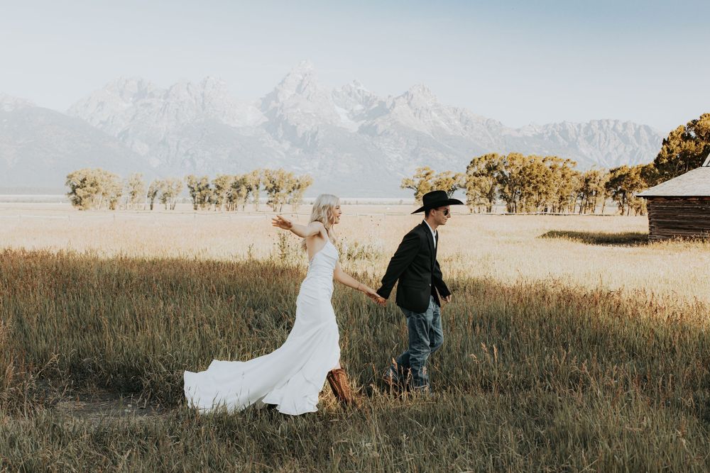 A couple walks together through a golden grass field at sunset during a romantic outdoor photo session.