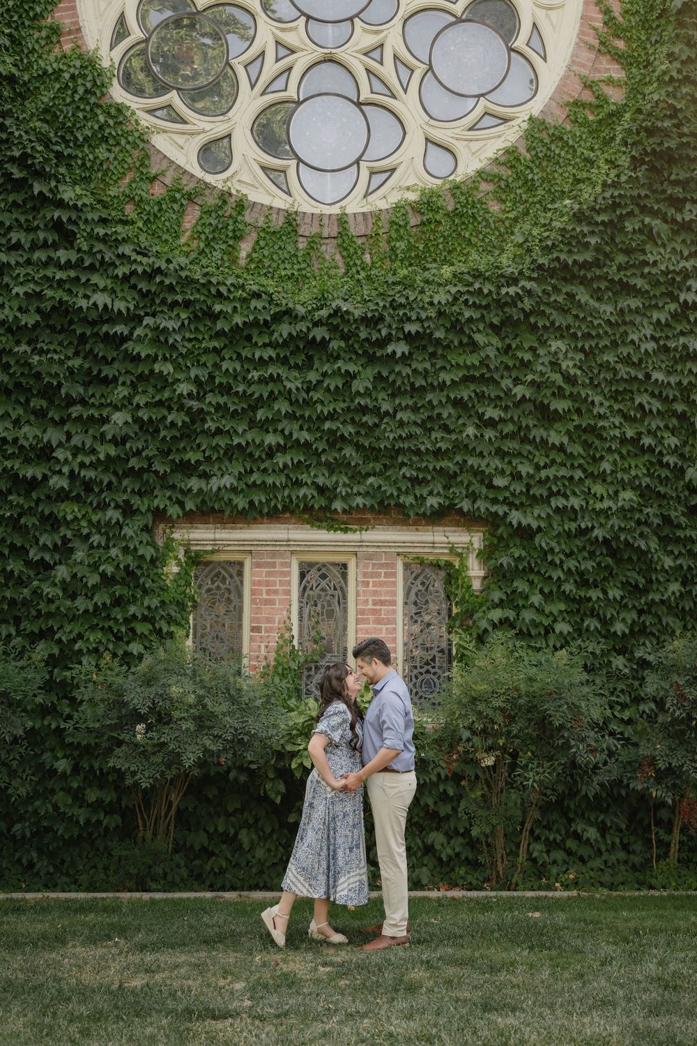 A couple shares an intimate moment together in a garden setting with ivy-covered walls and ornate architectural details.