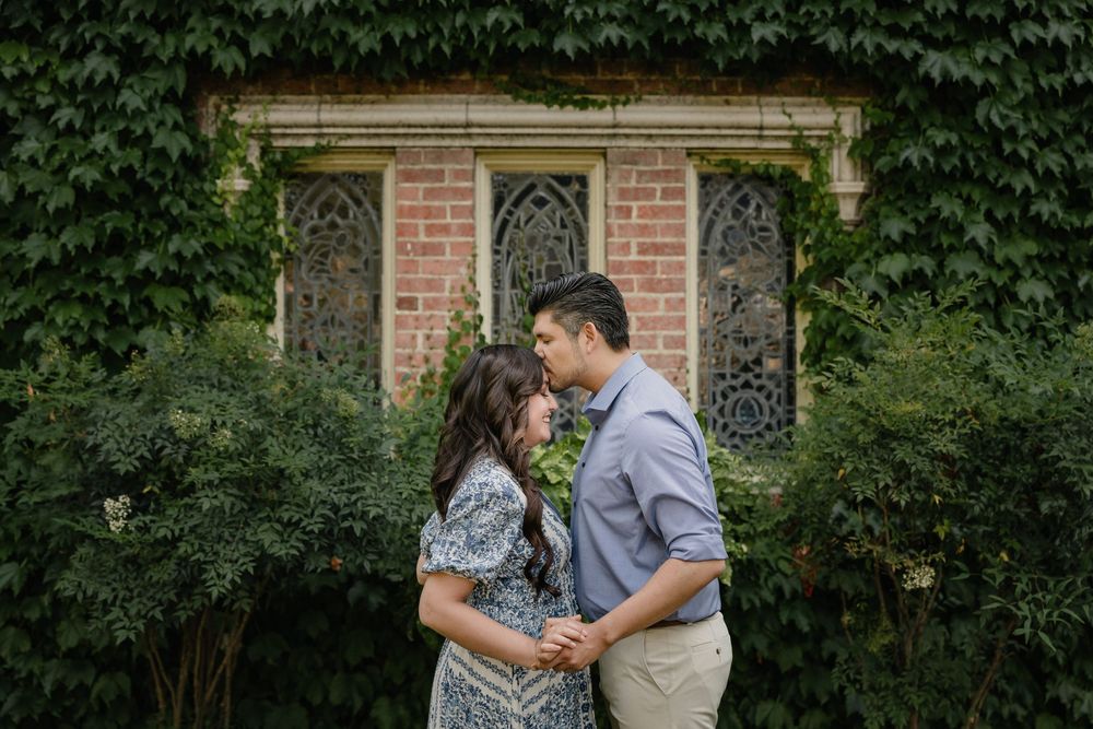 A couple shares a romantic moment in front of an ivy-covered brick building during a summer engagement photo session.