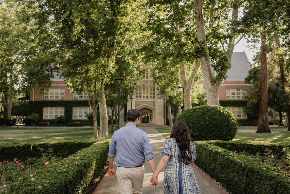 Couple walks together holding hands along a tree-lined path in a serene park setting during a sunny day.