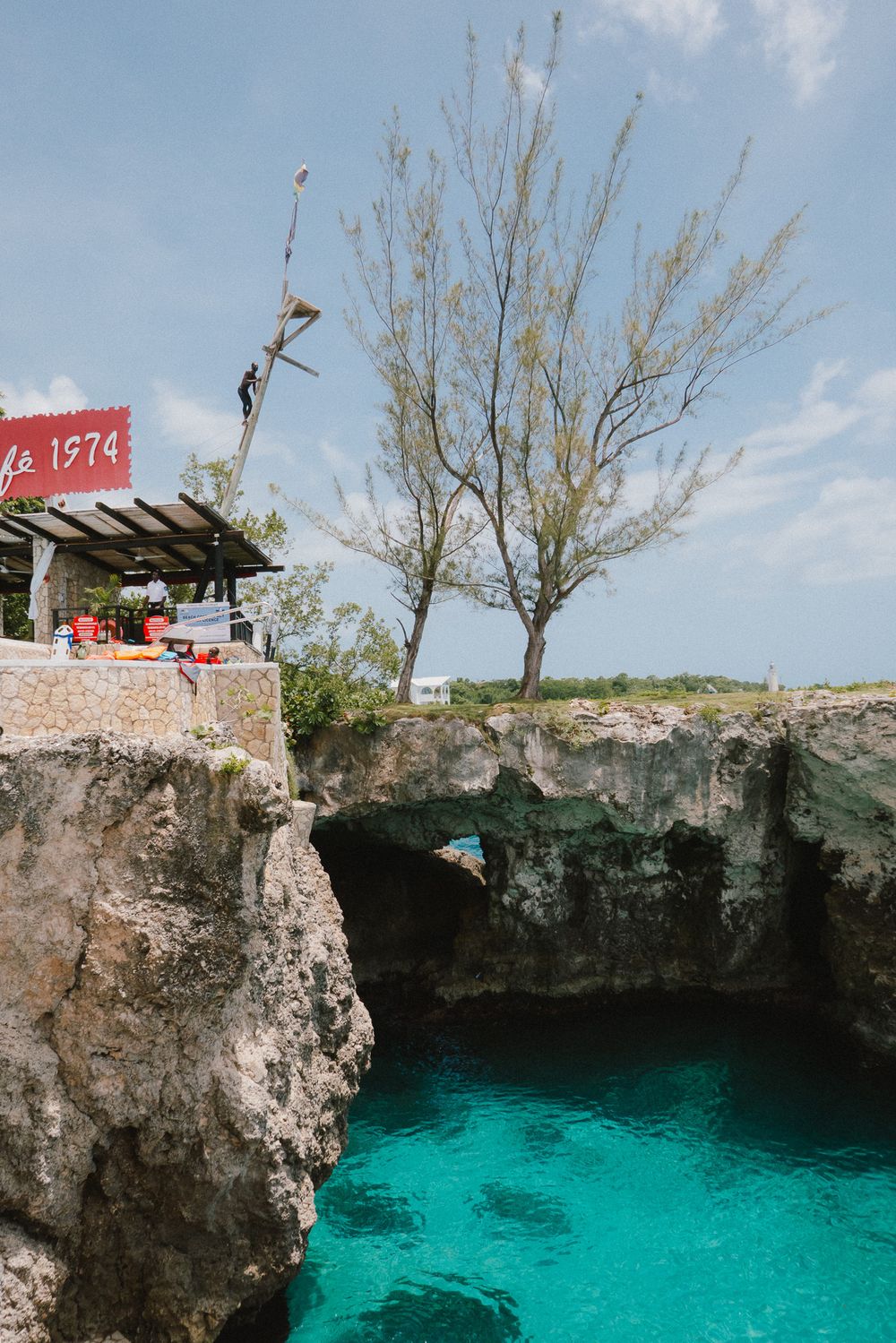 A person dives into the crystal clear turquoise waters of a natural limestone rock pool on a sunny day.