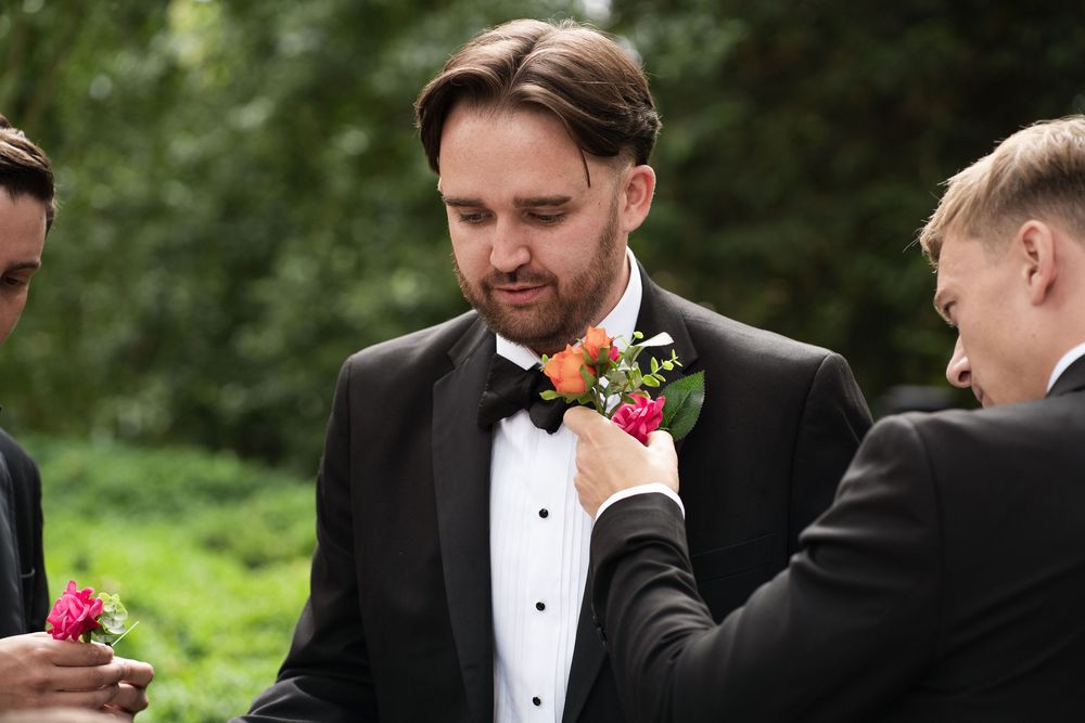A group in formal black tuxedos and ties gather outdoors for what appears to be a wedding celebration.