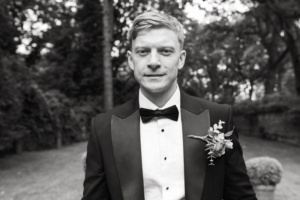 A formal portrait series of a person in a black tuxedo and bow tie against a natural outdoor backdrop.