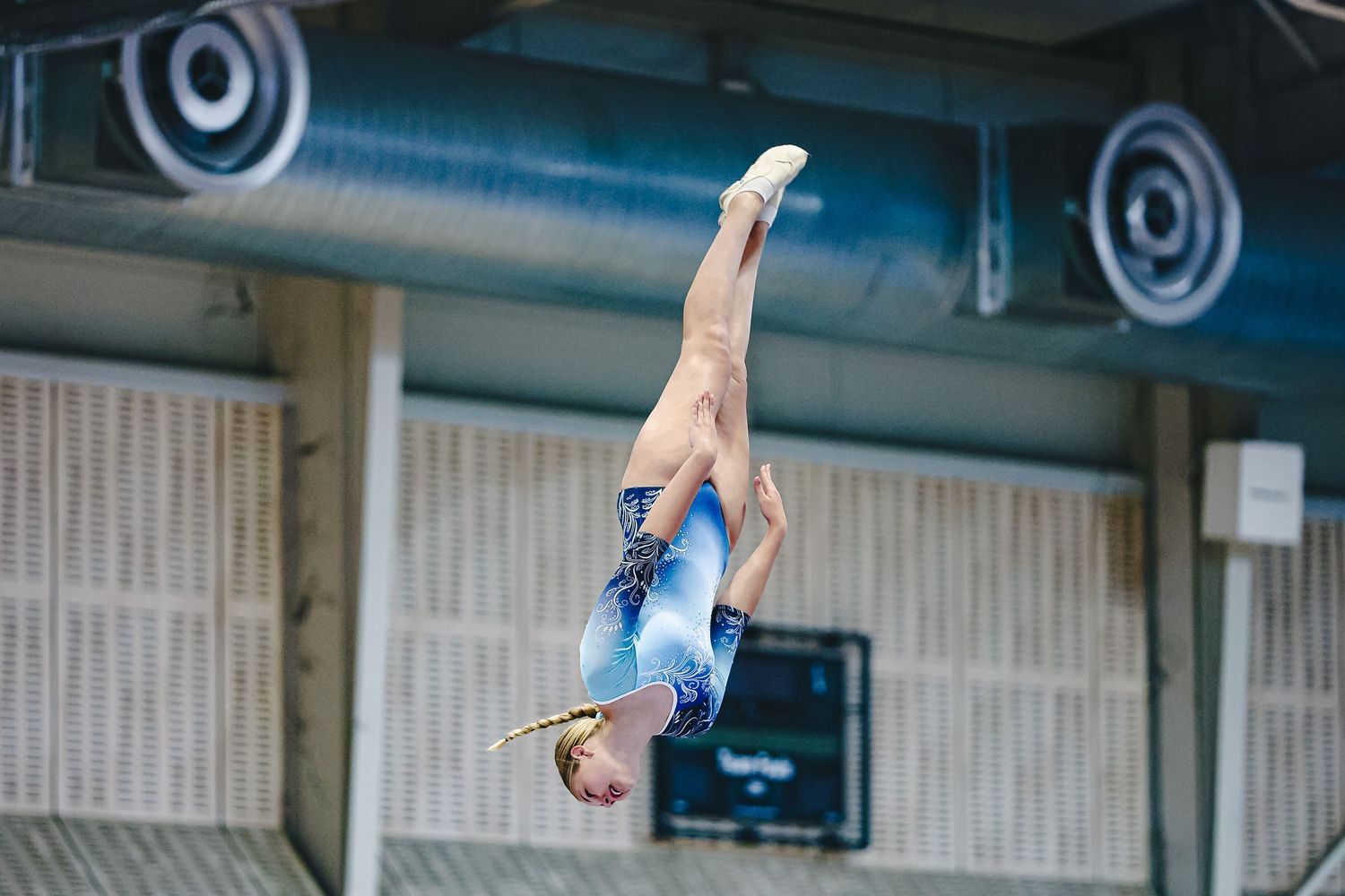 A gymnast performs a backward somersault sequence with precise form in a gymnastics training facility.