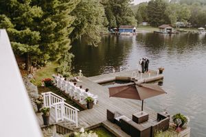 A lakeside wedding venue with a white deck and wooden dock surrounded by pine trees and calm waters.