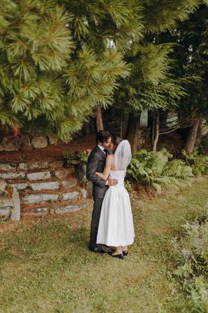 A wedding couple sharing an intimate moment among pine trees in a garden setting.