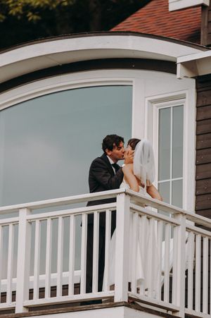 A romantic moment shared on a white-railed balcony of a lakeside venue.