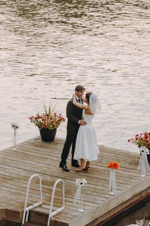 A couple shares an intimate moment on a decorated dock with floral arrangements during a waterfront ceremony.