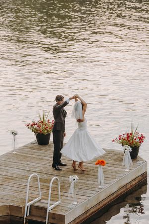 A couple exchanges rings during an intimate lakeside dock ceremony with floral decorations.
