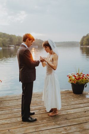 A couple shares a romantic moment on a wooden dock with flowers and lake views.