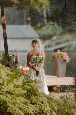 A serene wedding scene with floral decorations and pine trees framing a lakeside dock.