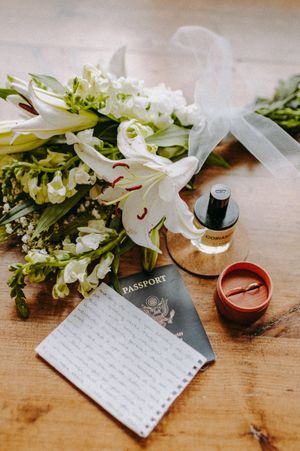 Wedding details flatlay with flowers, passport, and handwritten notes on wooden surface.