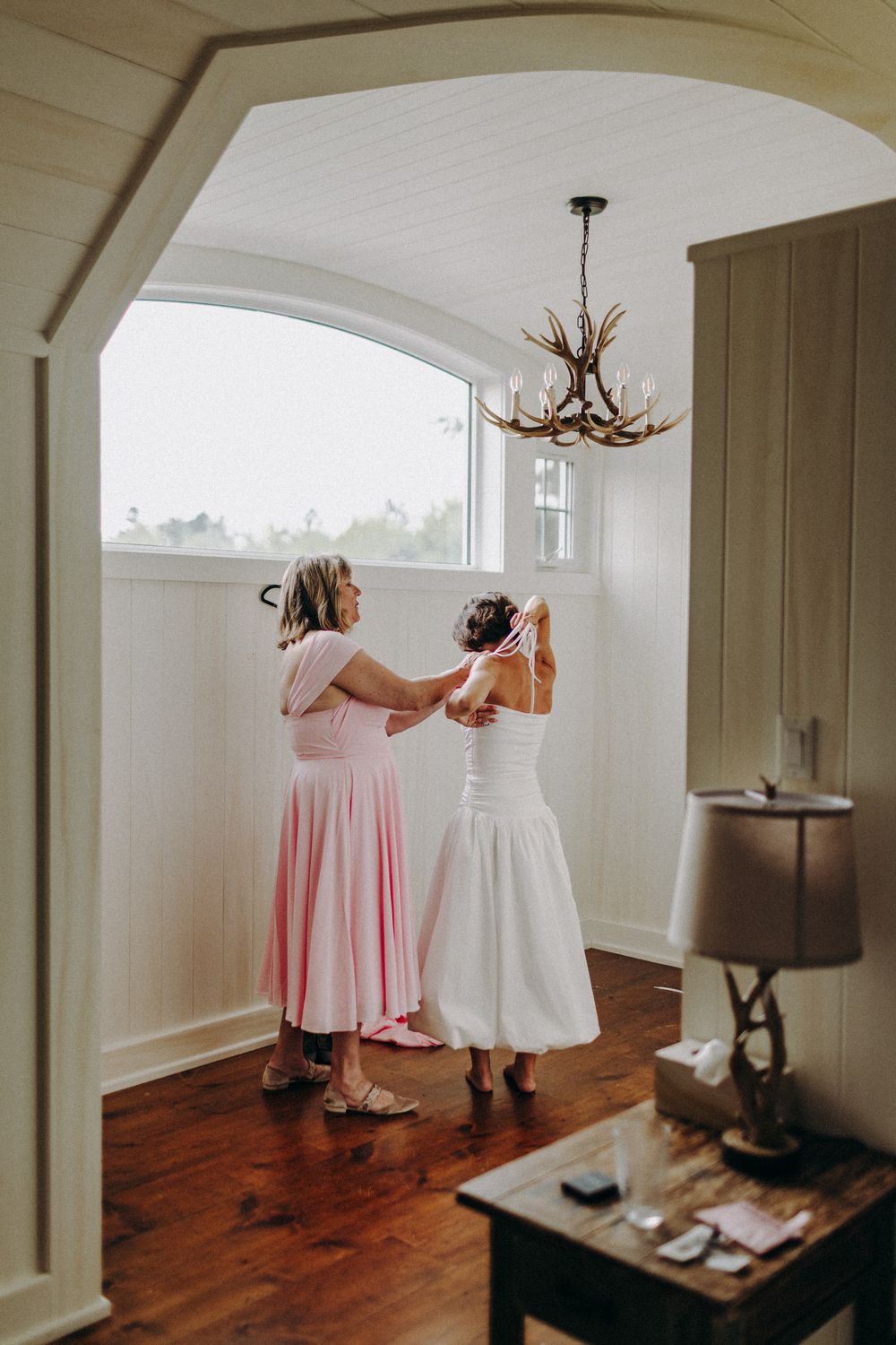 Interior wedding preparation scene with white arched doorways and hardwood floors.